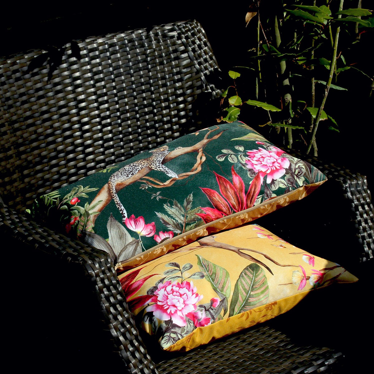 Leopard Jungle Polyester Cushion in gold and green shown on a rattan chair, printed with a leopard on a branch, tropical leaves and pink peonies, outdoor setting.