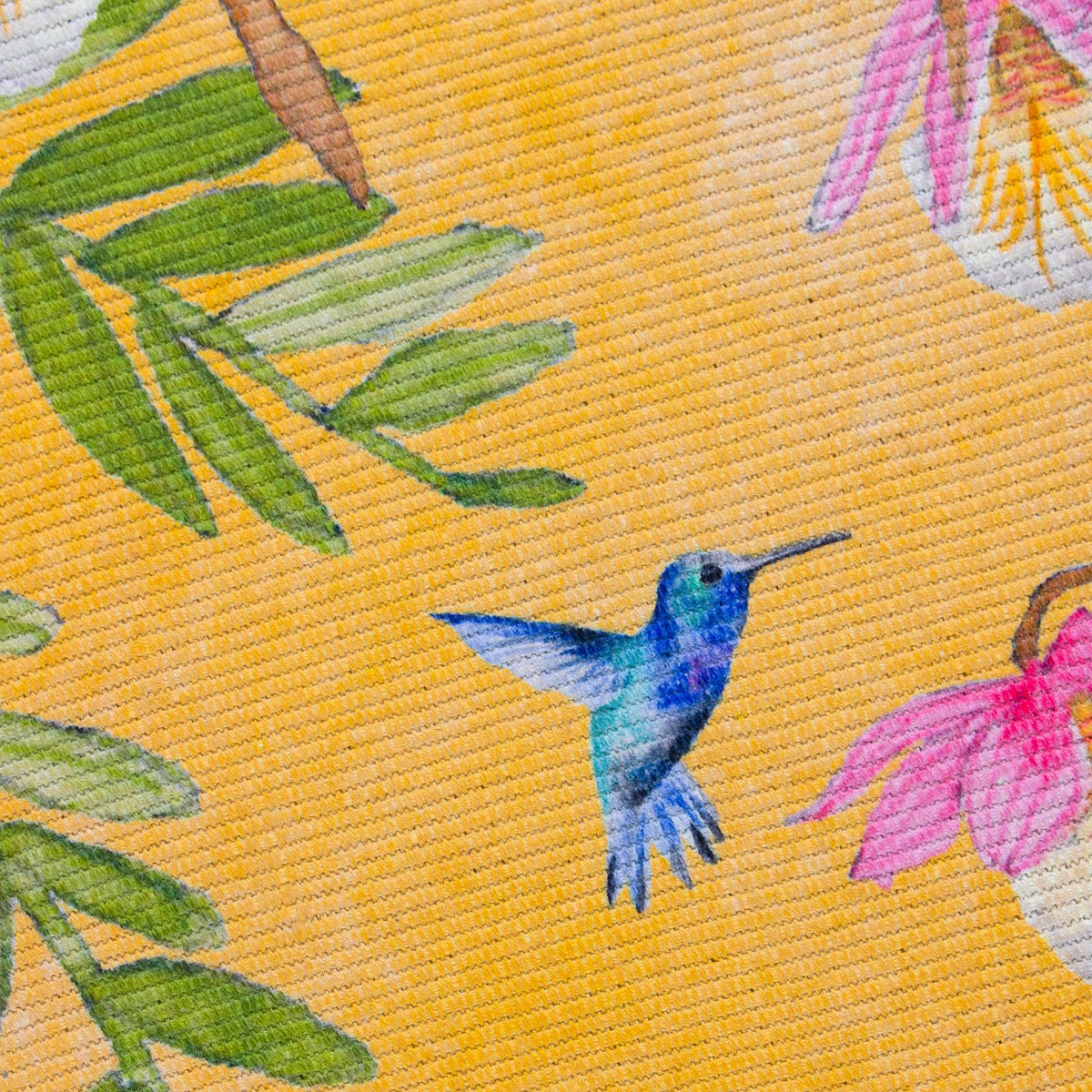 Close-up of the Leopard Animal Polyester Rug in ochre, showing a hummingbird, green foliage, and pink blooms printed on a woven yellow flatweave base.
