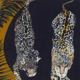 Leopardis reversible polyester cushion, close-up of two prowling leopards printed in black and gold on a dark background with amber palm fronds at the edge.