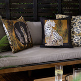 Leopardis reversible polyester cushion in black and gold on an outdoor sofa, showing a printed leopard trio design beside a seated leopard cushion and leopard-print scatter cushions.