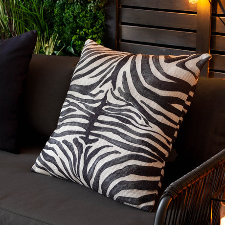 Leopardis Reversible Polyester Cushion in black and cream zebra print, shown on a dark outdoor sofa with woven basketweave texture visible.