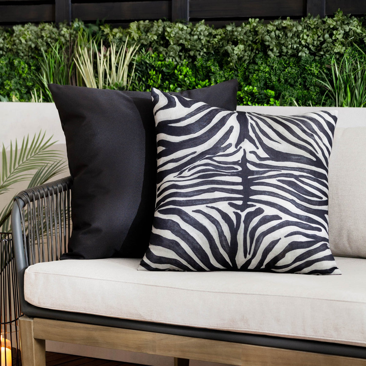 Leopardis reversible polyester cushion in zebra print, black and cream, shown reverse side in plain black on an outdoor sofa with cream cushions.