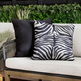 Leopardis reversible polyester cushion in zebra print, black and cream, shown reverse side in plain black on an outdoor sofa with cream cushions.