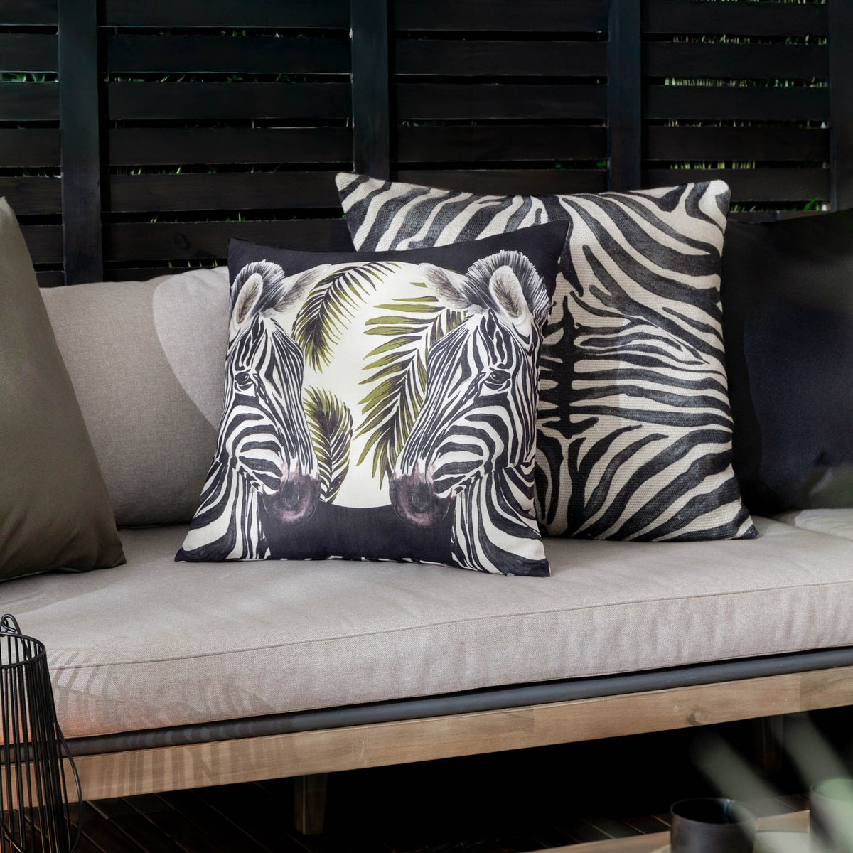 Leopardis reversible polyester cushion with zebra print design and palm leaf motif, shown among monochrome cushions on an outdoor sofa.