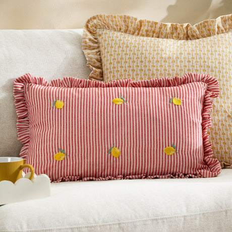 Rectangular cushion in red and cream pinstripe polyester with ruffle-trimmed edges and embroidered yellow lemon motifs, styled on a sofa beside a floral yellow cushion.
