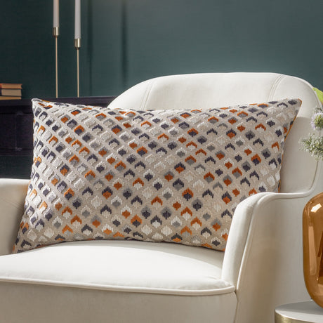 Lexington Jacquard Velvet Cushion in Ginger/Grey, a rectangular bolster with a woven diamond pattern in rust, charcoal and cream, styled on a cream armchair.