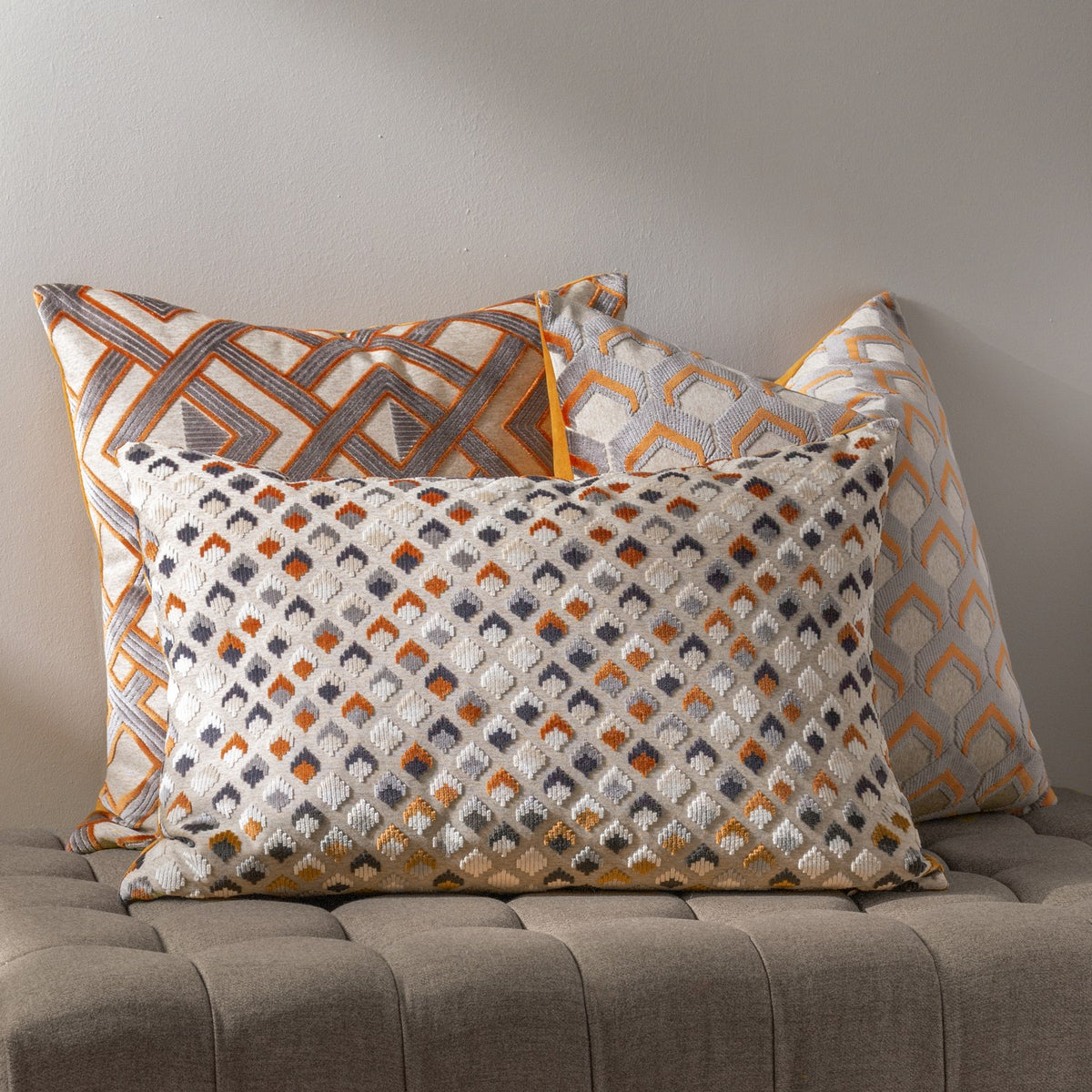 Lexington rectangular jacquard velvet cushion in ginger and grey diamond pattern, shown with matching geometric-print cushions on a grey bench against a neutral wall.