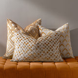 Lexington Jacquard Velvet Cushion in Gold with a raised diamond lattice pattern in gold, ochre and grey, shown among patterned cushions on a burnt orange upholstered bench.