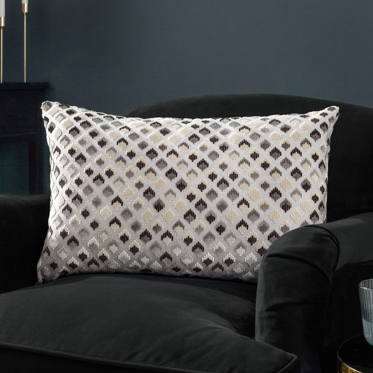 Lexington Jacquard Velvet Cushion in Grey/Black, a rectangular bolster with diamond-patterned woven velvet face, shown on a black velvet armchair in a dark-toned room.