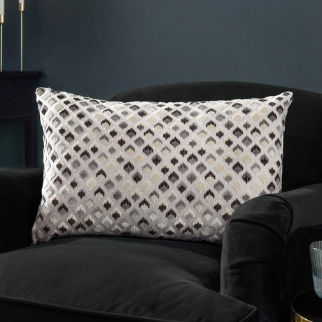 Lexington Jacquard Velvet Cushion in Grey/Black, a rectangular bolster with diamond-patterned woven velvet face, shown on a black velvet armchair in a dark-toned room.