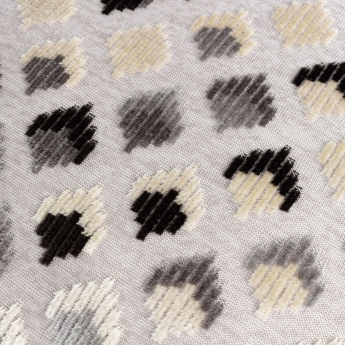 Lexington jacquard velvet cushion close-up showing a grid of small diamond motifs in cream, gold-beige, grey and black on a pale woven ground.