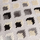 Lexington jacquard velvet cushion close-up showing a grid of small diamond motifs in cream, gold-beige, grey and black on a pale woven ground.