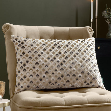 Lexington Jacquard Velvet Cushion in Warm Taupe with a diamond-patterned gold, charcoal and grey design, styled on a beige tufted armchair.