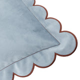 Close-up of the Lil Scallop Plain Velvet Cushion in blue, showing its velvet fabric corner with a scalloped edge and contrasting brown trim on a white background.