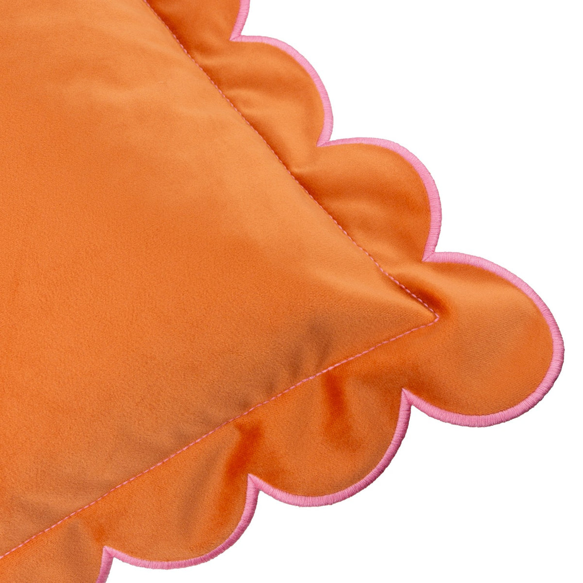 Close-up of the Lil Scallop velvet cushion in orange, showing its scalloped edge with contrast pink stitching, on a plain white background.