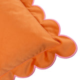 Close-up of the Lil Scallop velvet cushion in orange, showing its scalloped edge with contrast pink stitching, on a plain white background.