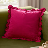 Lil Scallop Plain Velvet Cushion in pink with red scalloped edge trim, shown on a green sofa in a living room setting.