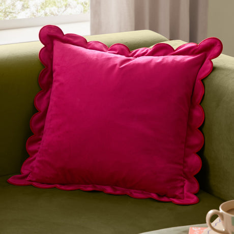Lil Scallop Plain Velvet Cushion in pink with red scalloped edge trim, shown on a green sofa in a living room setting.