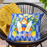 Limoncello Abstract Polyester Cushion in blue, printed with lemons, leaves and Limoncello bottles on a geometric diamond ground, shown on a black wicker chair with a mustard throw.
