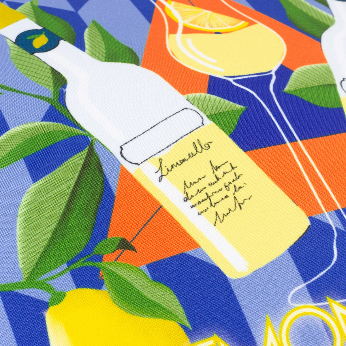 Close-up of the Limoncello Abstract Polyester Cushion in blue, showing a Limoncello bottle label, lemons and green leaves on a blue diamond-patterned fabric with orange accents.