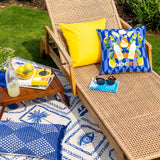 Limoncello Abstract Polyester Cushion in blue with orange reverse, featuring lemon and bottle motifs, styled on a wicker garden lounger outdoors.