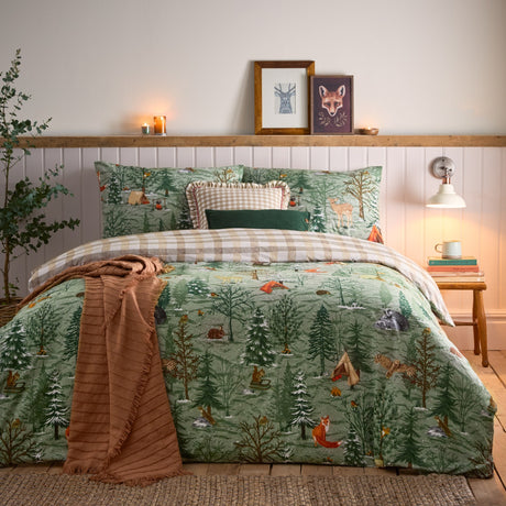 Lodge Wood cotton duvet cover set in green, styled on a bed with woodland animal and tree print, gingham reverse, and matching pillowcases in a bedroom setting.
