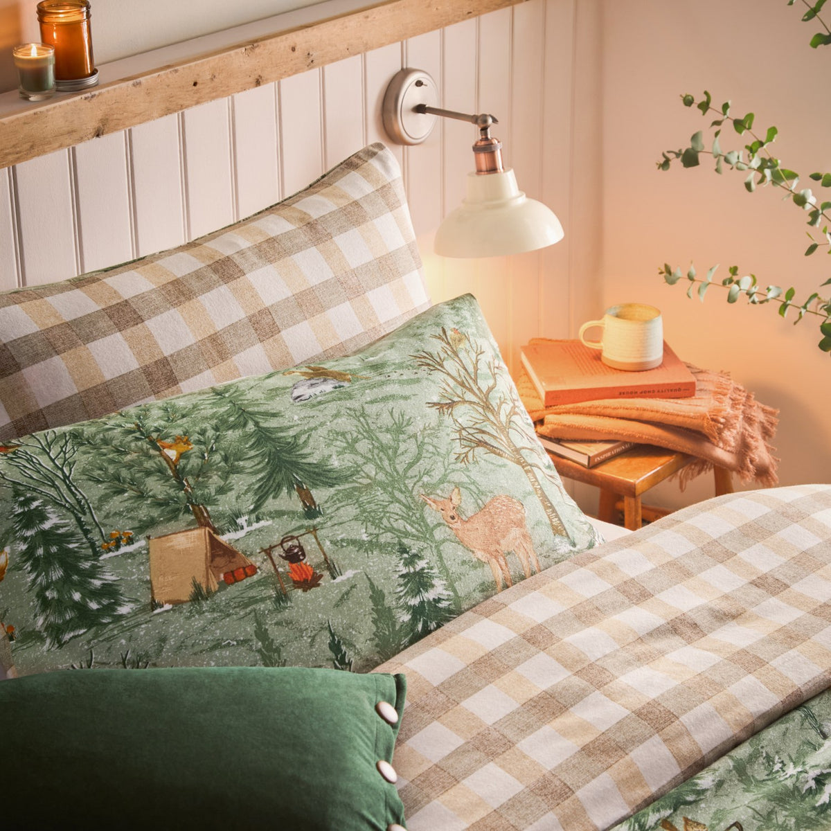 Lodge Wood Cotton Animal Duvet Cover Set in green on a bed, featuring an embroidered woodland scene with deer, trees and tents, paired with beige check pillowcases in a bedroom setting.
