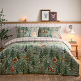 Lodge Wood Cotton Animal Duvet Cover Set in green, styled on a bed with matching pillowcases showing a woodland print of foxes, deer, owls and fir trees in a bedroom setting.
