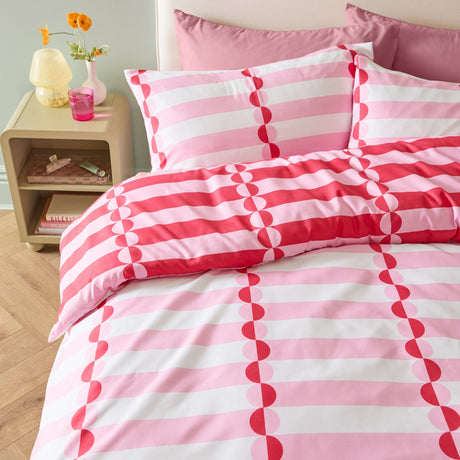 Lottie Reversible Geometric Duvet Cover Set in pink and red on a bedroom bed, featuring striped fabric with vertical half-circle patterns and matching pillowcases.