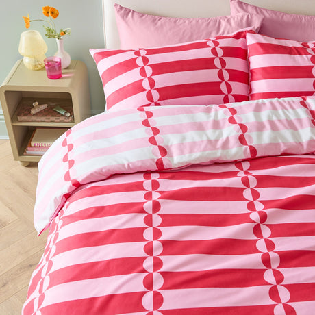 Lottie Reversible Geometric Duvet Cover Set in red and pink, shown on a bed with matching pillowcases featuring striped and half-circle patterns in a bedroom setting.