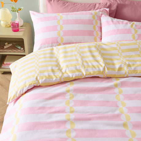 Lottie reversible duvet cover set on a bed, showing pink and white stripe with yellow disc pattern on the cover and yellow striped pillowcases with matching design.