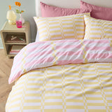 Lottie reversible duvet cover set on a bed, yellow and white striped side with disc pattern shown, pink striped pillowcase reverse visible, in a bedroom setting.