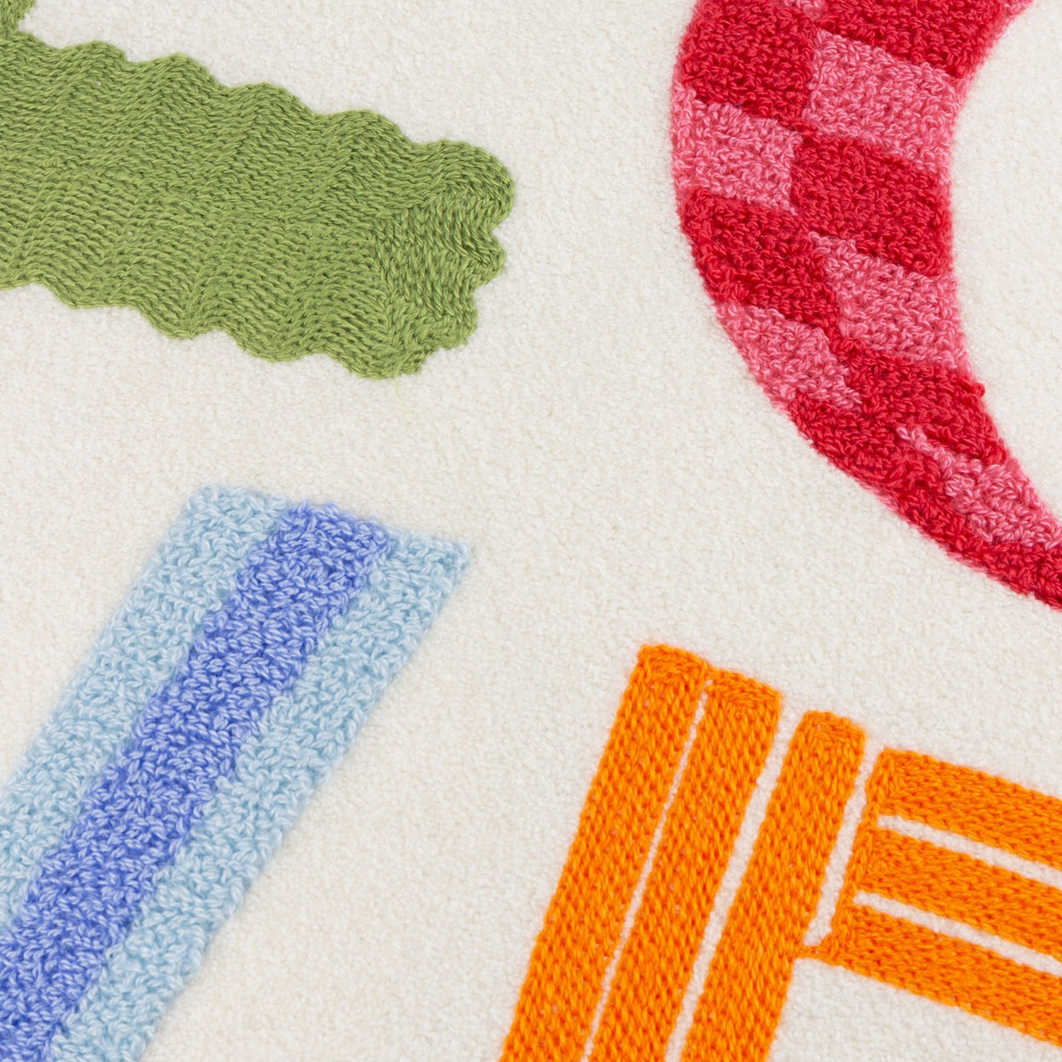 Close-up of the Love Tuft Embroidered Polyester Cushion on cream micro boucle, showing tufted LOVE letters in green, red-pink checked, blue ridged, and orange textures.