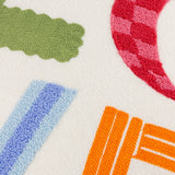 Close-up of the Love Tuft Embroidered Polyester Cushion on cream micro boucle, showing tufted LOVE letters in green, red-pink checked, blue ridged, and orange textures.
