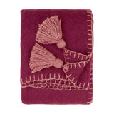 Folded Lowen wool-blend throw in deep berry red with dusky pink cotta blanket-stitch trim and jumbo corner tassels, shown on a plain white background.