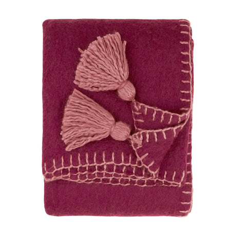 Folded Lowen wool-blend throw in deep berry red with dusky pink cotta blanket-stitch trim and jumbo corner tassels, shown on a plain white background.