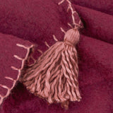 Close-up of the Lowen wool-blend throw in berry red with a dusky pink (cotta) blanket-stitch trim and jumbo corner tassel detail.
