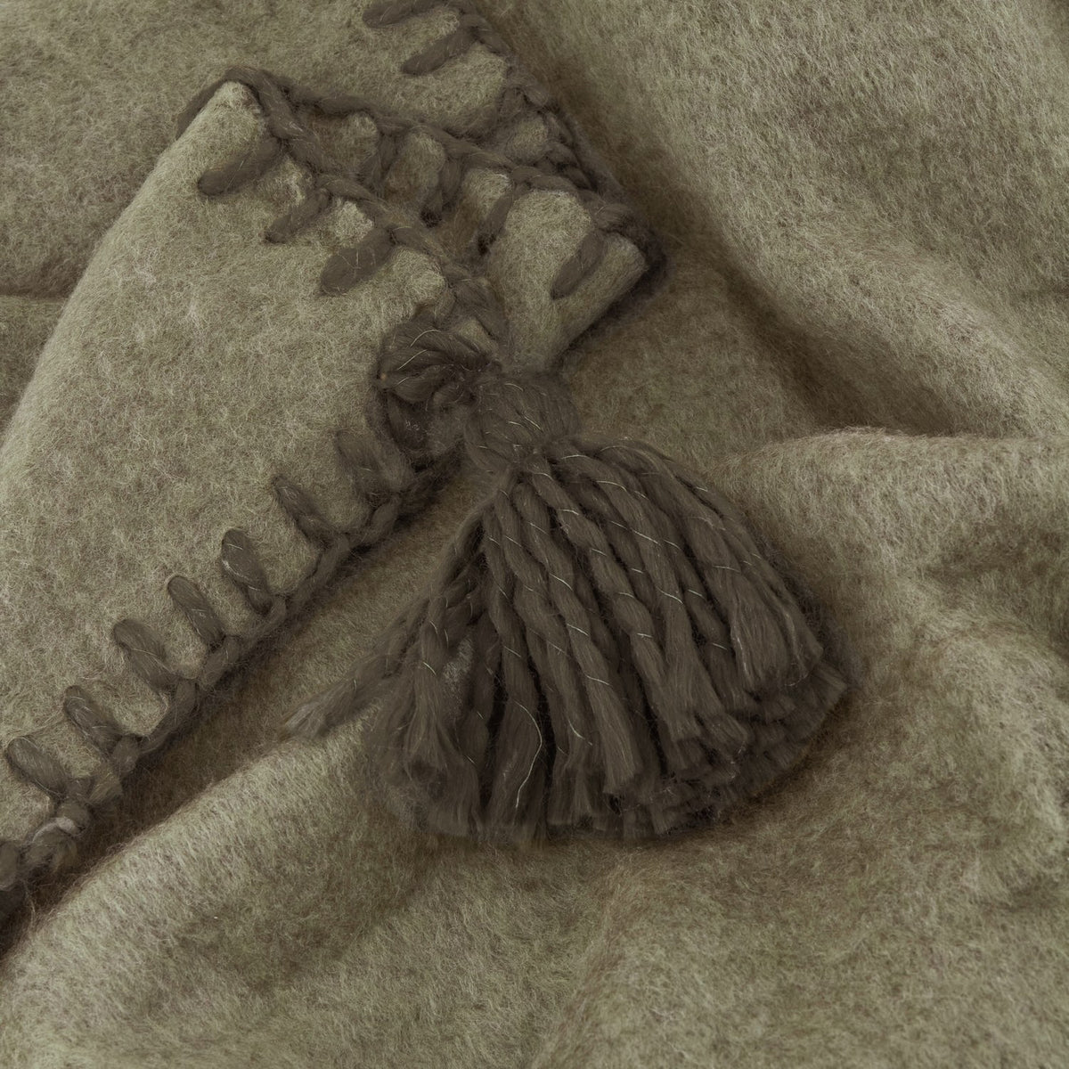 Close-up of the Lowen wool blend throw in moss green, showing a whipstitched edge and matching tassel detail on brushed, felted fabric.