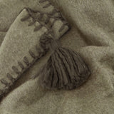 Close-up of the Lowen wool blend throw in moss green, showing a whipstitched edge and matching tassel detail on brushed, felted fabric.