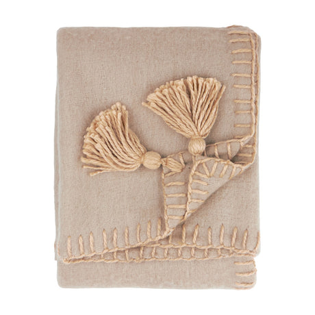 Lowen Wool Plain Polyester Throw in natural beige, folded, with hand-worked blanket-stitch edging and jumbo corner tassels, shown on a plain white background.