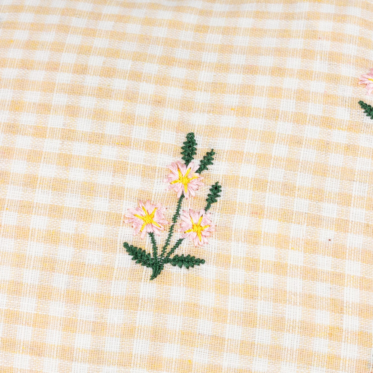 Les Petite Fleurs Gingham Cotton Cushion in natural, close-up of the check fabric with a small embroidered pink, yellow and green flower motif.