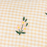Les Petite Fleurs Gingham Cotton Cushion in natural, close-up of the check fabric with a small embroidered pink, yellow and green flower motif.