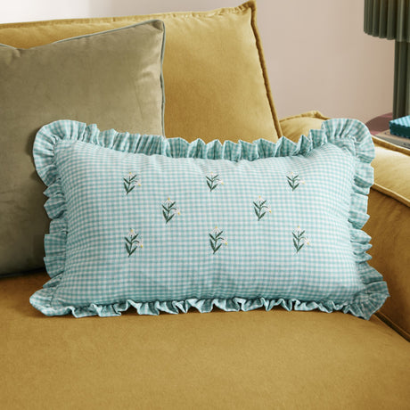 Rectangular Les Petite Fleurs cushion in spring green gingham cotton with embroidered floral sprigs and a frilled edge, shown on a mustard velvet sofa.
