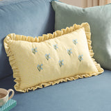 Rectangular yellow and white gingham cotton cushion with frilled trim, embroidered blue flower sprigs, styled on a blue sofa with a teal cushion behind.