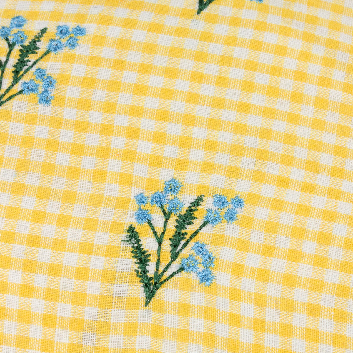 Close-up of Les Petite Fleurs Gingham Cotton Cushion in yellow, showing yellow and white check cotton fabric with embroidered blue flower sprigs on green stems.