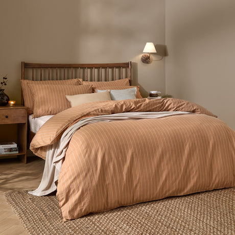 Linear Stripe Cotton Printed Duvet Cover Set in Demerara Sugar, a brown duvet with fine white pinstripes and matching pillowcases, shown on a bed with a dark wood headboard.