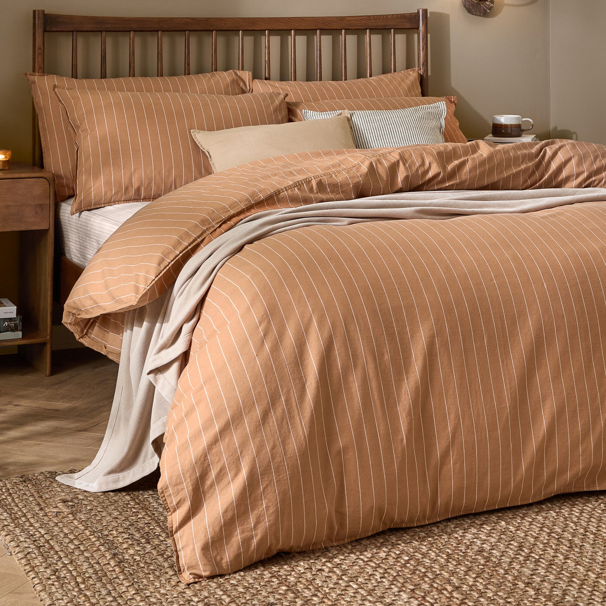 Linear Stripe Cotton Printed Duvet Cover Set in Demerara Sugar, brown with fine white stripes, styled on a bed with matching pillowcases in a wooden-framed bedroom setting.