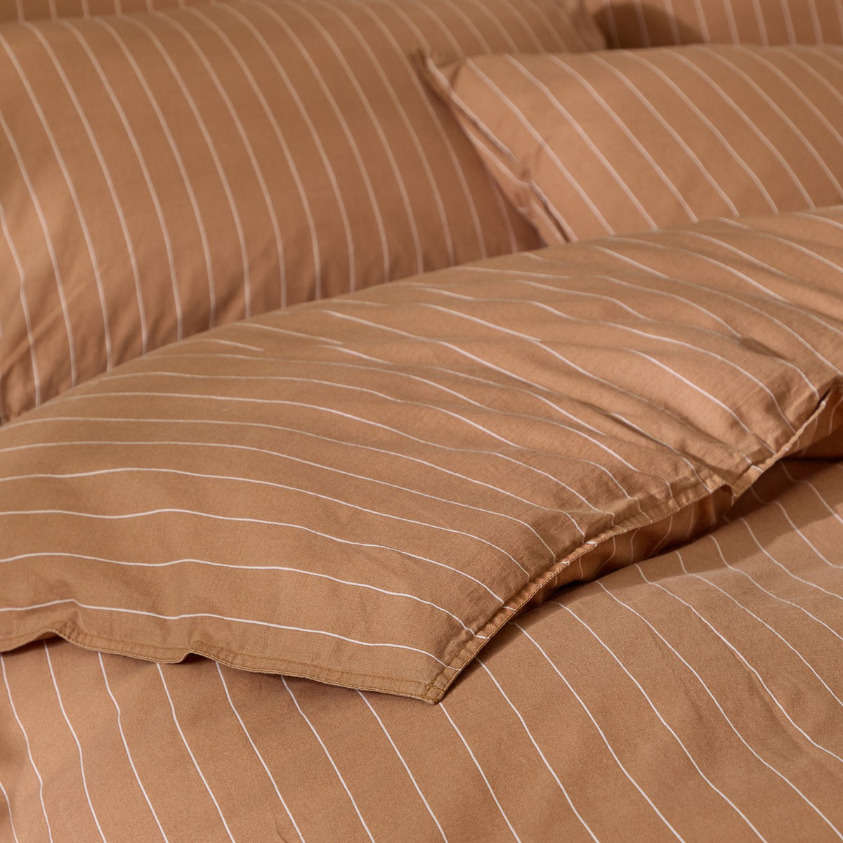 Close-up of the Linear Stripe Cotton Printed Duvet Cover Set in Demerara Sugar, showing fine white pinstripes on a warm brown cotton duvet cover and matching pillowcase.