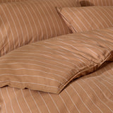 Close-up of the Linear Stripe Cotton Printed Duvet Cover Set in Demerara Sugar, showing fine white pinstripes on a warm brown cotton duvet cover and matching pillowcase.