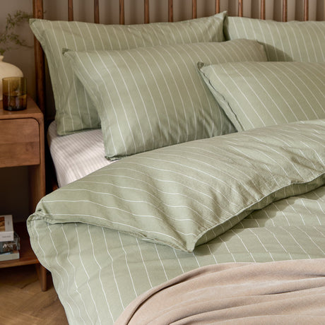 Linear Stripe Cotton Printed Duvet Cover Set in Forest, showing a green cotton duvet cover and pillowcases with fine white pinstripes, styled on a bed with a wooden headboard.